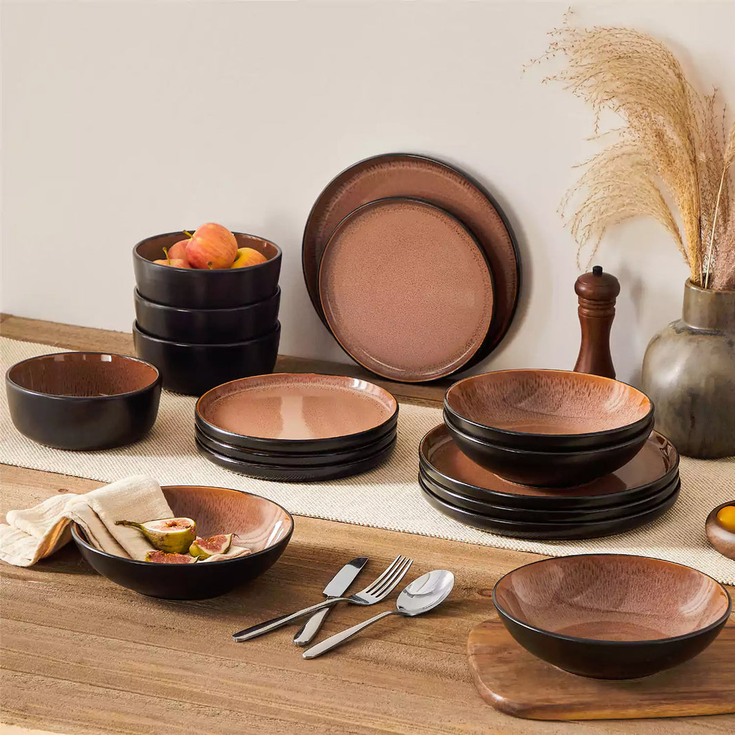 Amber 16-piece red dinnerware set stacked on a warm, gray wooden dining table, complemented by figs and apples for a cozy, rustic touch.