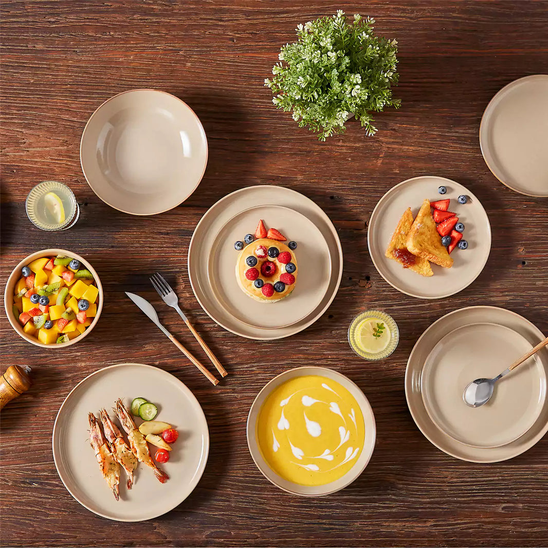 Playa 16-piece glossy dinnerware set in caramel with pumpkin soup, fruit salad, baked shrimp, and soufflé on a dark wooden table.