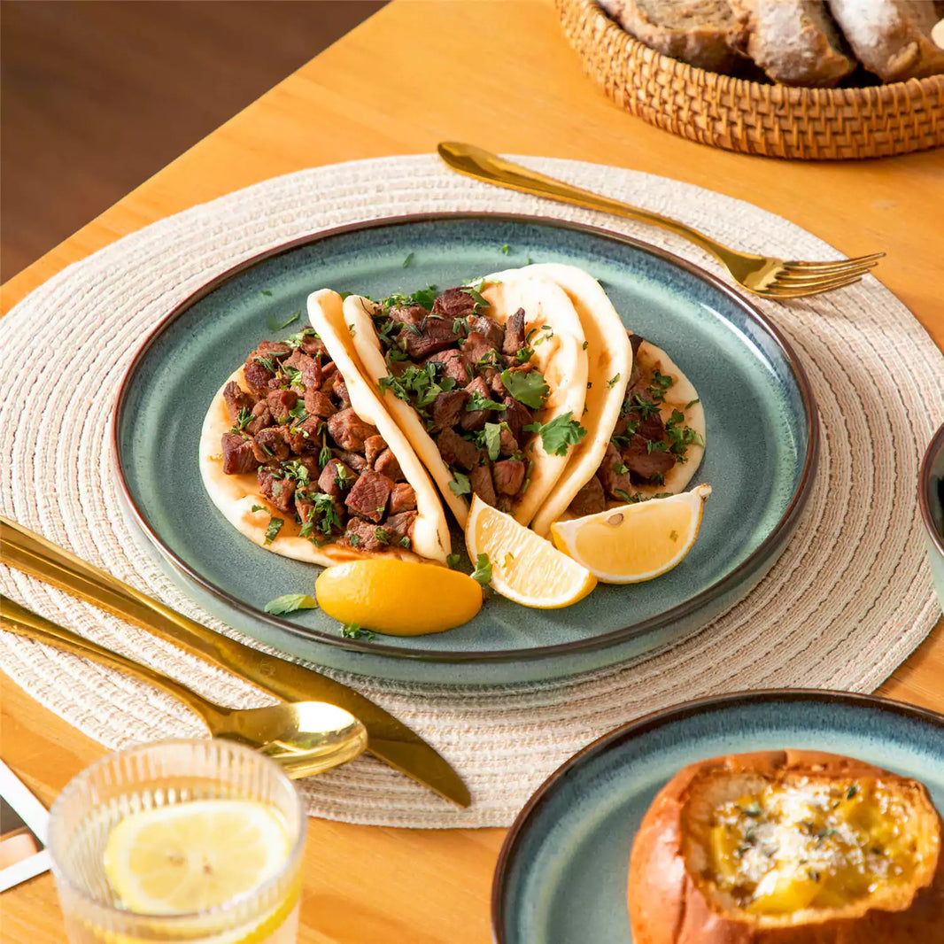Sata green lipped-edge dinnerware close-up with tacos, pumpkin bread and lemonade on brown wood dining table.
