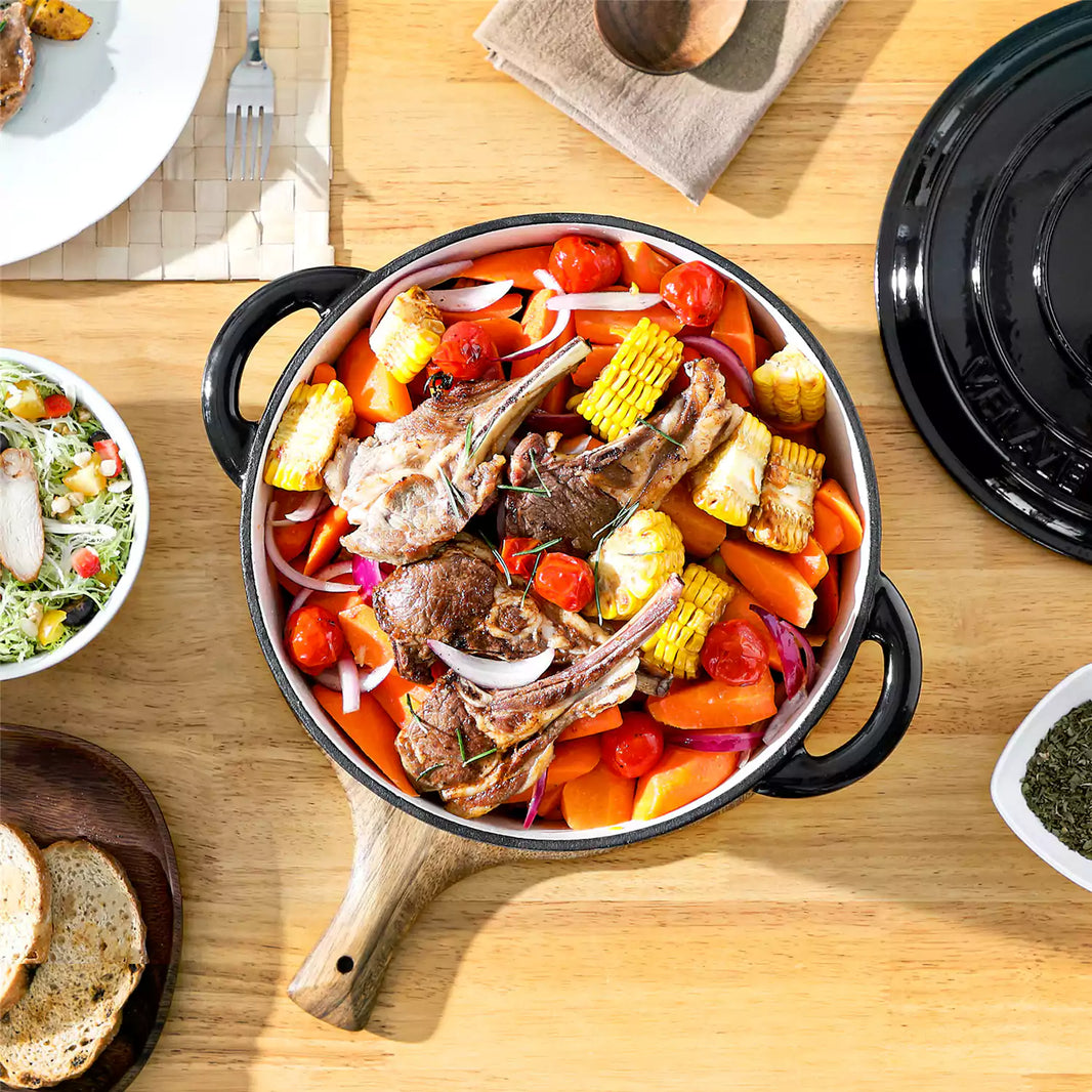 Casets Black 6.5qt enameled cast iron dutch oven with roasted lamb chops, carrots and corn, served with fresh salad and bread cubes.